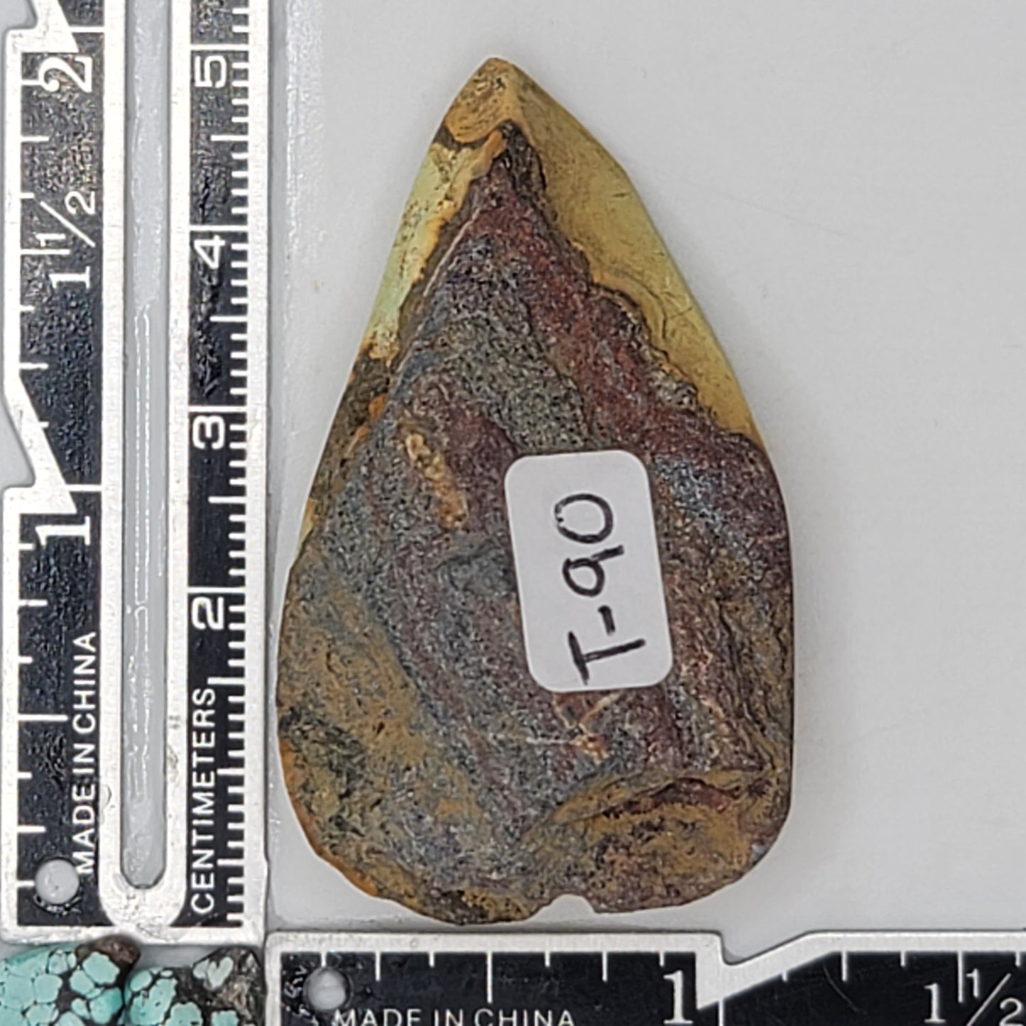 A natural turquoise stone weighing 24 grams, featuring earthy golden hues with bold dark matrix patterns and organic textures. The stone measures approximately 5.5 cm x 3 cm x 0.6 cm, displayed with a ruler for scale. Available for purchase at www.naturalturquoise.com, ideal for lapidary and jewelry projects.