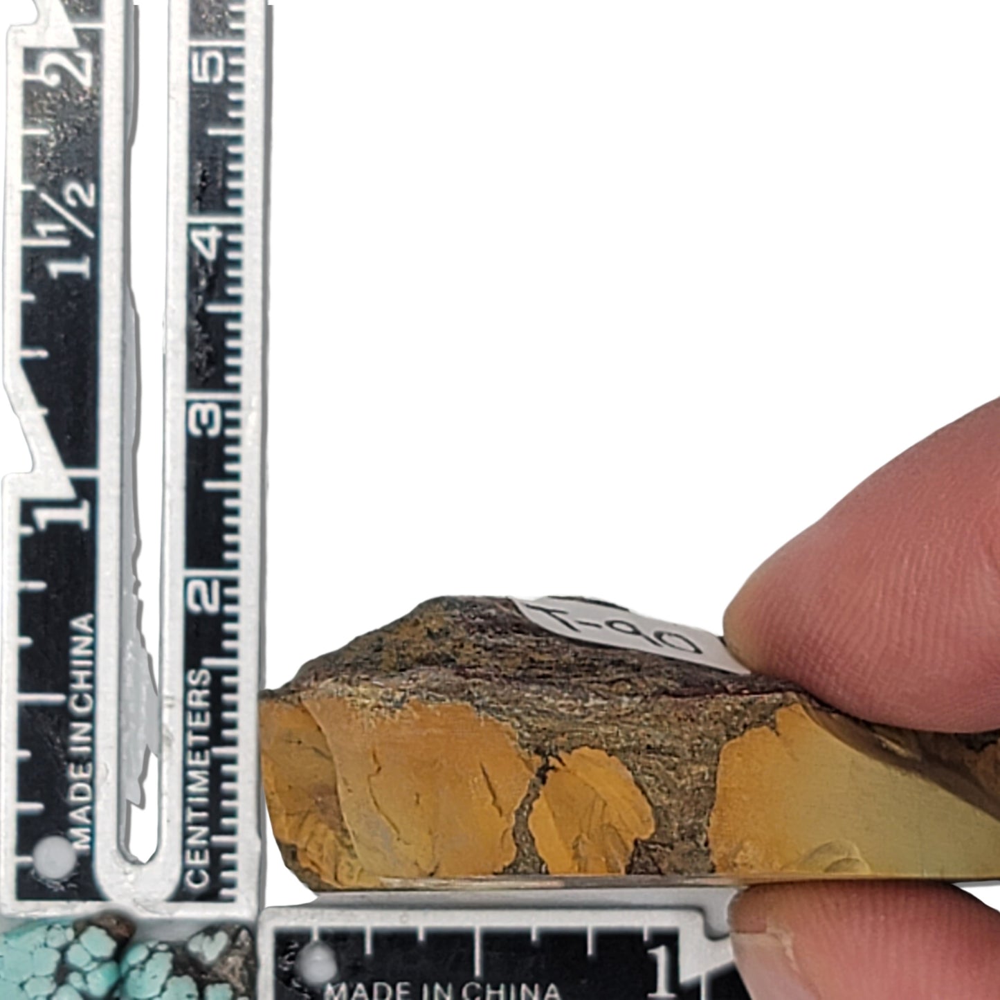 A natural turquoise stone weighing 24 grams, featuring earthy golden hues with bold dark matrix patterns and organic textures. The stone measures approximately 5.5 cm x 3 cm x 0.6 cm, displayed with a ruler for scale. Available for purchase at www.naturalturquoise.com, ideal for lapidary and jewelry projects.